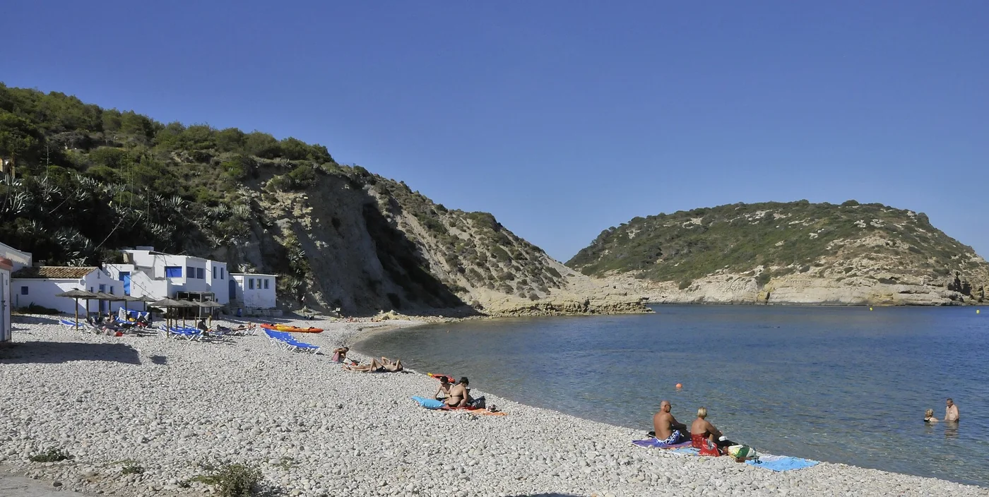 Turkusowa woda zatoczki Cala Portitxol w Jávei z kajakami na brzegu